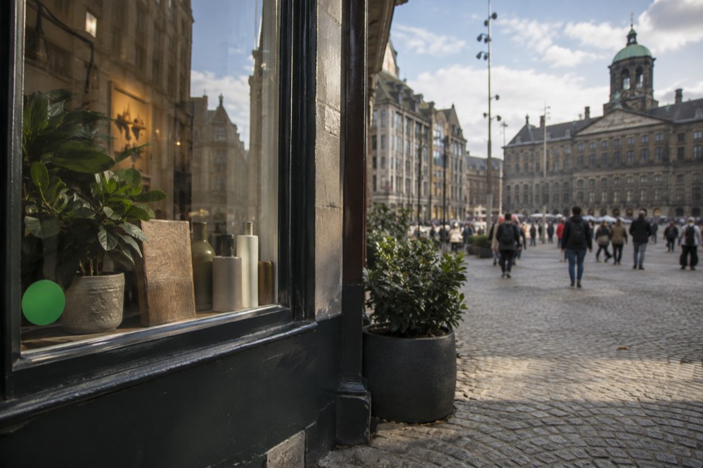A small Amsterdam shopfront window with a green sticker and a quiet interior