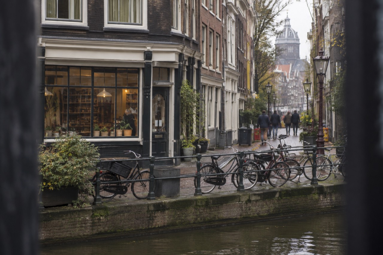 A narrow Amsterdam street with a small shopfront and bicycles parked along the canal edge