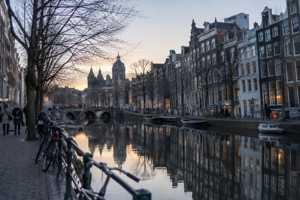 Canal houses reflected in still Amsterdam water at dusk