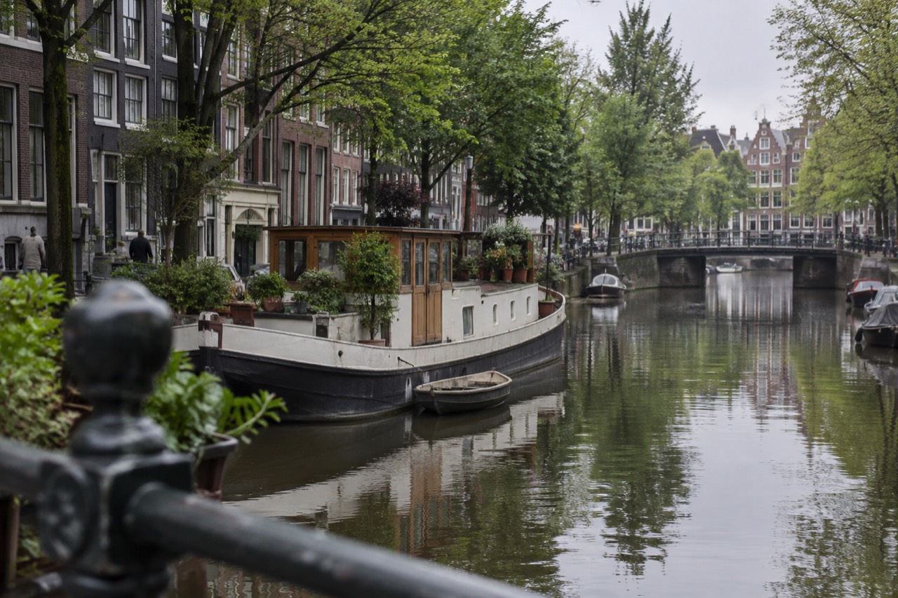 A houseboat moored on an Amsterdam canal with trees reflected in the water