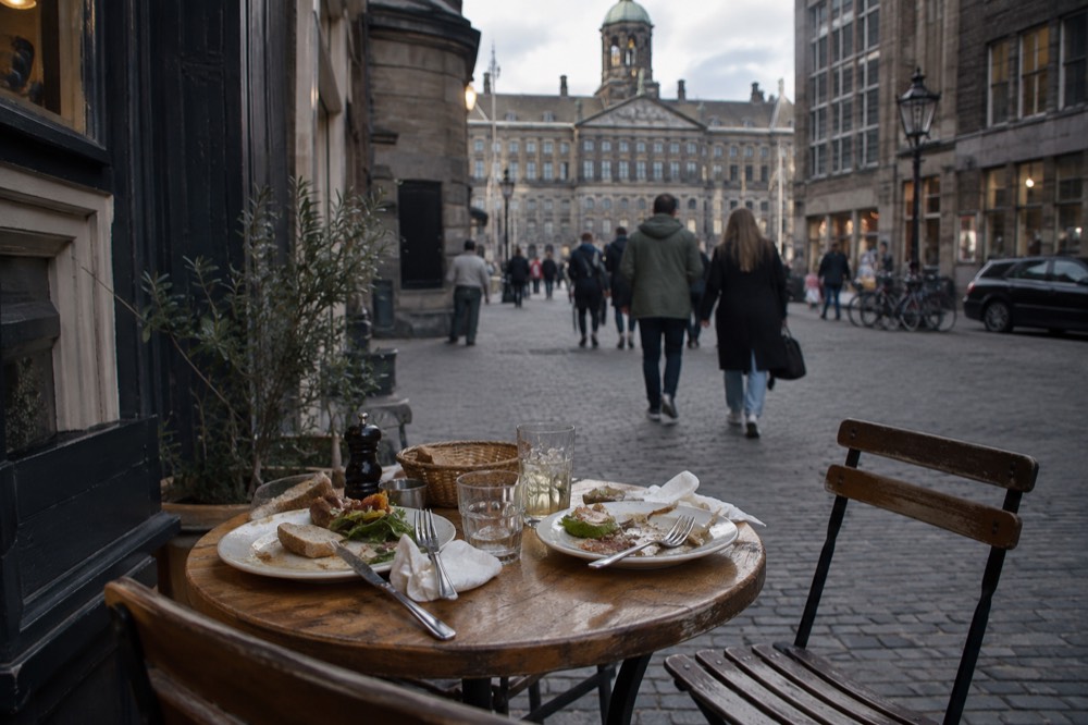 Outdoor table for two with plates of food on a quiet Amsterdam side street in the evening