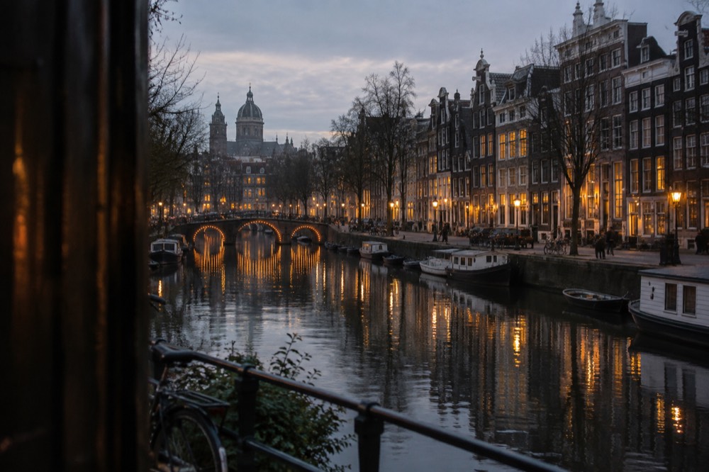 Illuminated Amsterdam canal at dusk with bridges and gabled houses reflected in still water