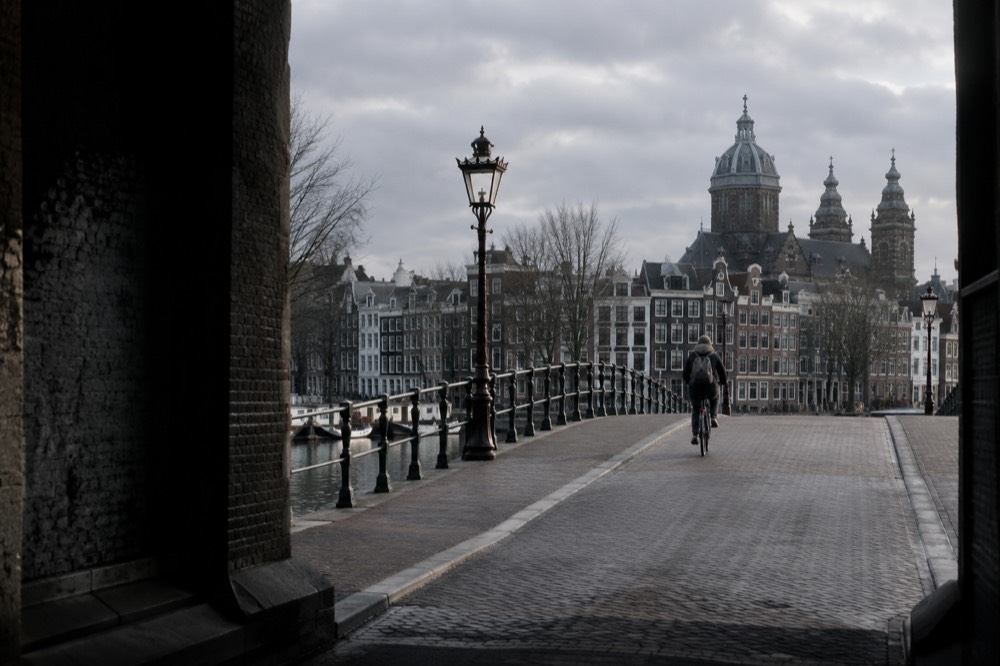 A cyclist crossing an empty Amsterdam bridge under a grey winter sky