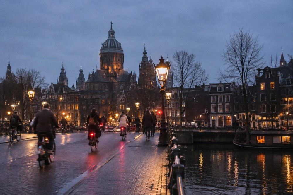 Cyclists with headlights crossing an Amsterdam bridge in early winter dusk