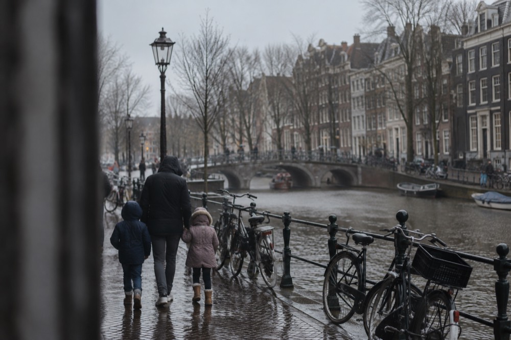 Families walking along a quiet Amsterdam canal with bicycles parked against a railing