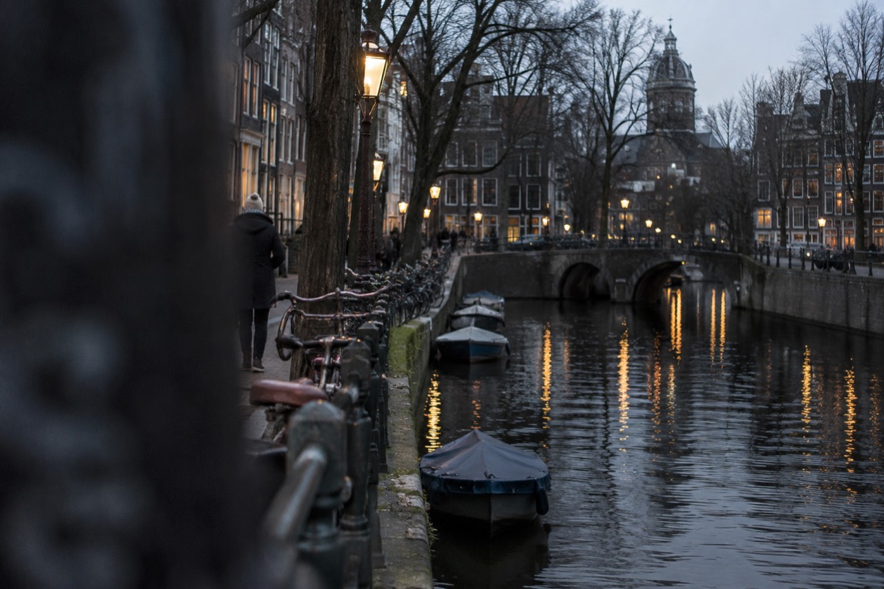 A quiet Amsterdam canal street in the evening with lamplight reflecting on the water