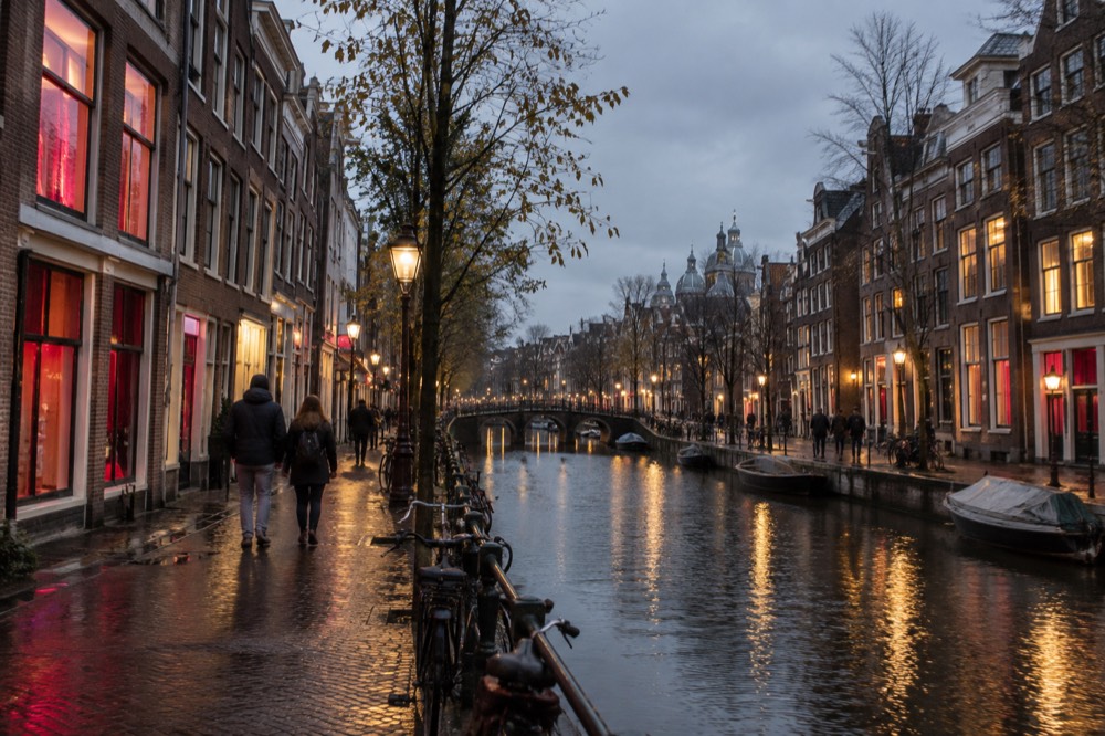Narrow Amsterdam canal street at dusk with old brick buildings and warm window light