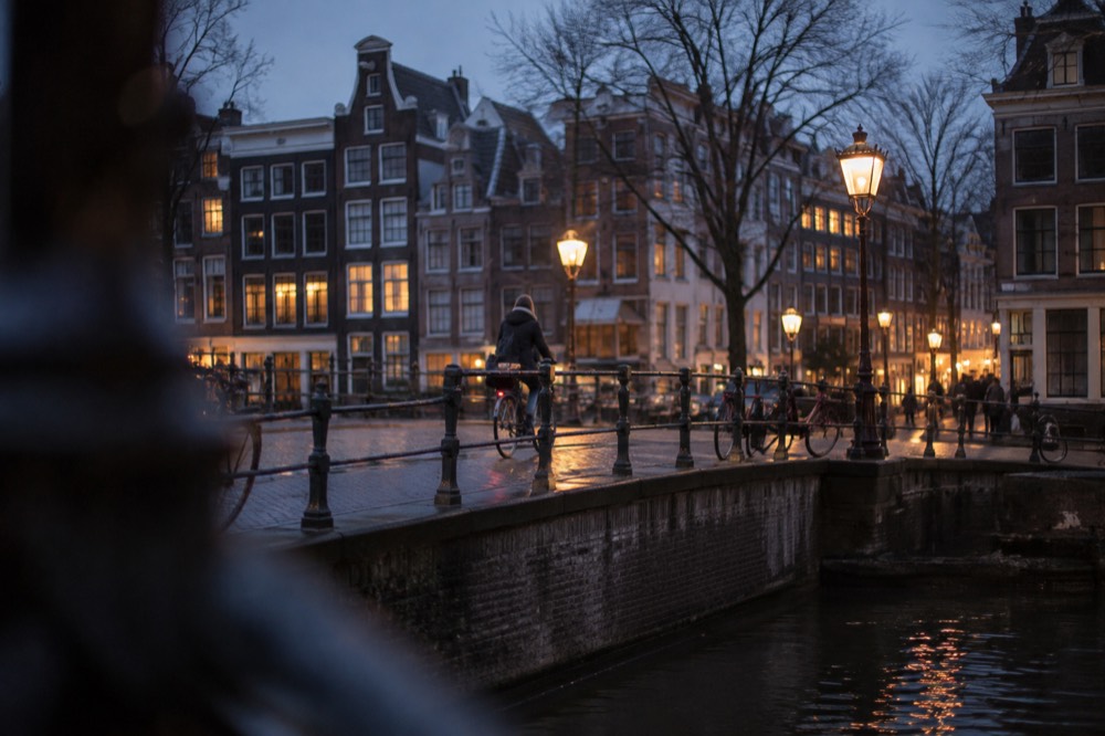 A cyclist riding through an Amsterdam street lined with canal houses