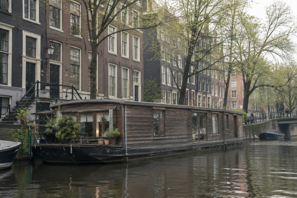 A historic wooden houseboat moored on an Amsterdam canal with brick facades behind it