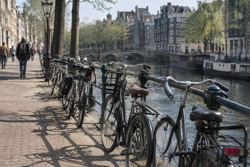 A row of bicycles parked against a railing beside an Amsterdam canal