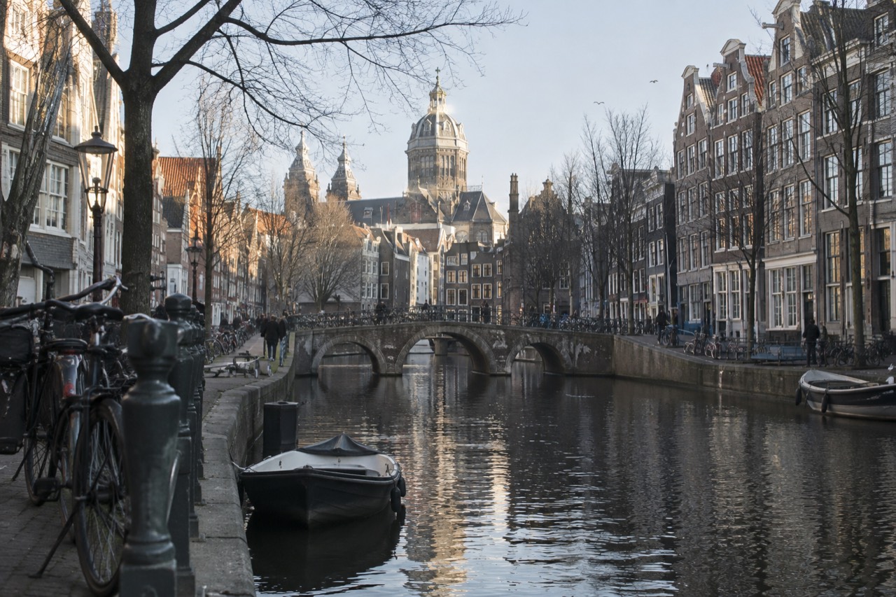 A quiet Amsterdam canal lined with traditional gabled houses and a small boat moored beside a brick quay.