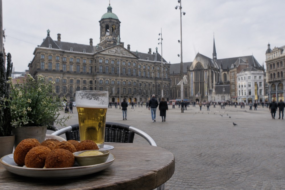 A plate of bitterballen with a small dish of mustard on a wooden cafe table beside a glass of beer