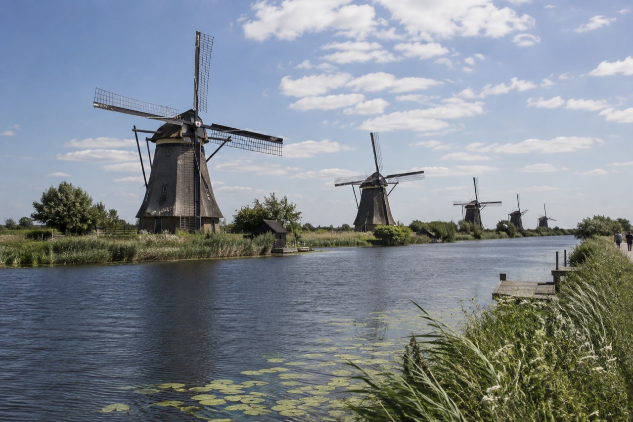 A row of historic Dutch windmills standing beside a green waterway under a wide sky