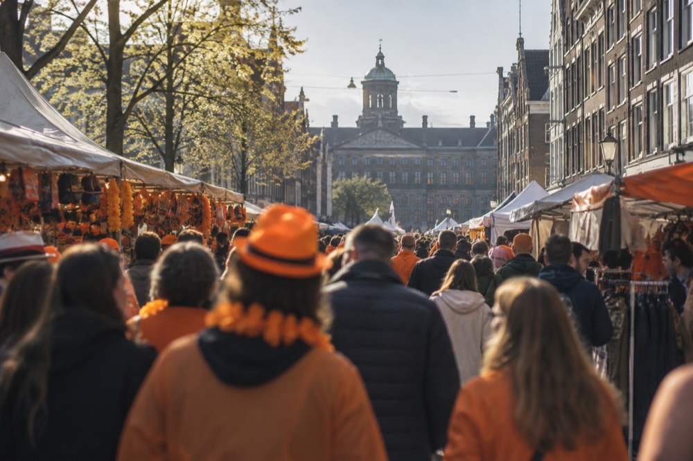 Crowds in orange clothing fill a narrow Amsterdam street lined with market stalls