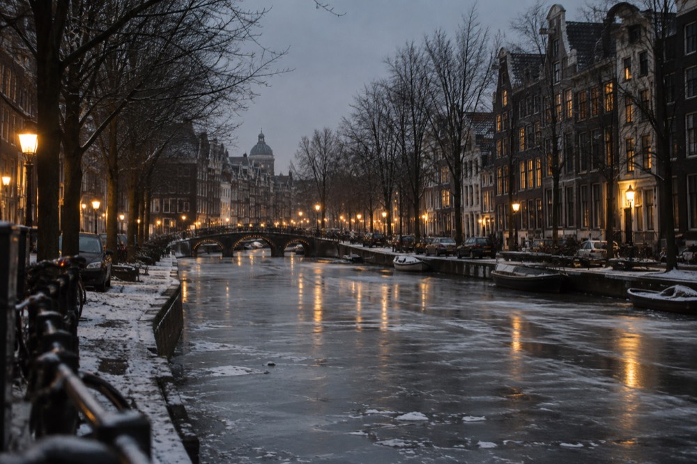 Amsterdam canal houses and a bridge under a pale winter sky with bare trees along the frozen water