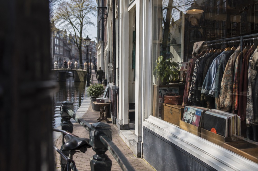 A vintage shop window displaying second-hand clothing and records on an Amsterdam canal street