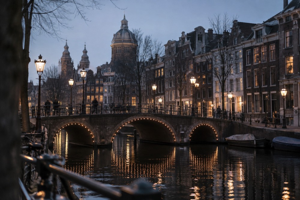 A canal bridge and street lamps reflecting in dark water during blue hour in Amsterdam
