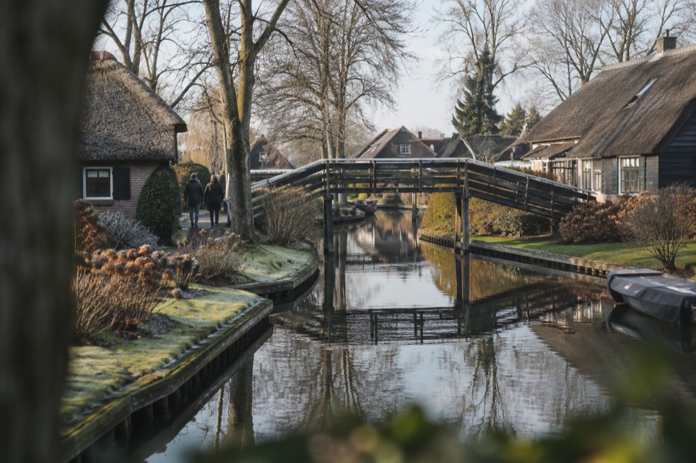 Thatched cottages reflected in a still Giethoorn canal with a wooden footbridge
