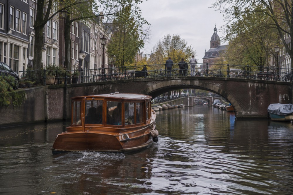 A classic wooden saloon boat passing under a low canal bridge in Amsterdam