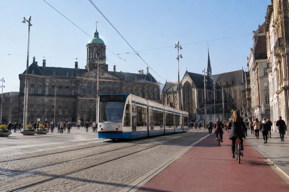 A tram moving along a street in central Amsterdam beside a red cycle lane