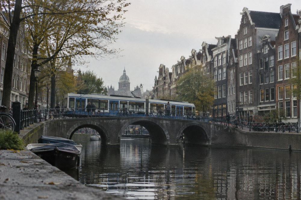 Amsterdam tram crossing a canal bridge with gabled houses on both sides