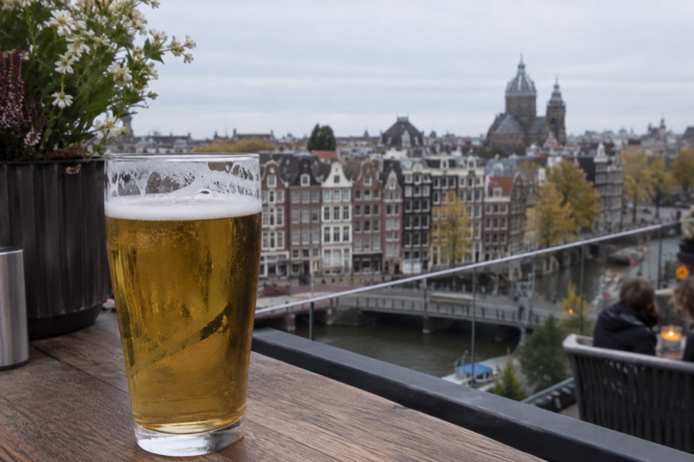 A glass of Heineken on a rooftop bar overlooking Amsterdam canal houses
