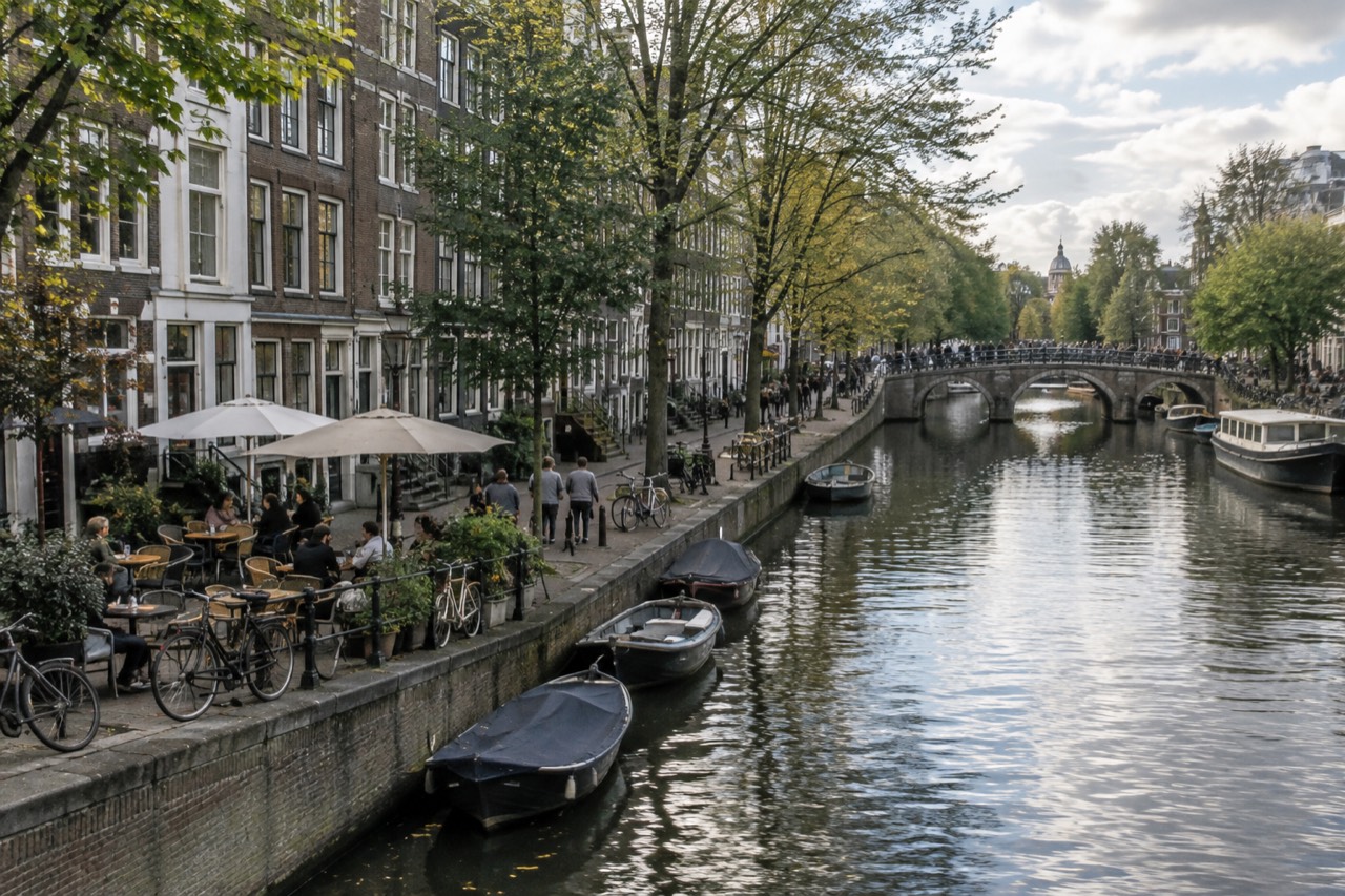 A canal-side street in Amsterdam with small café terraces and bicycles parked outside.