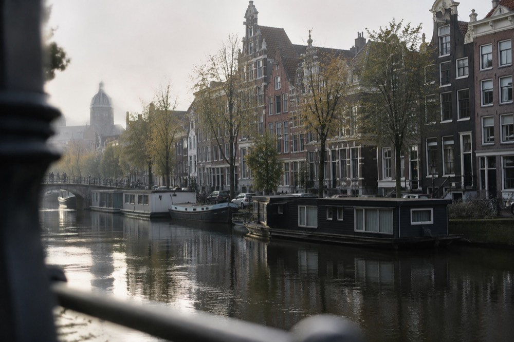 Row of narrow gabled canal houses along an Amsterdam gracht with houseboats moored below