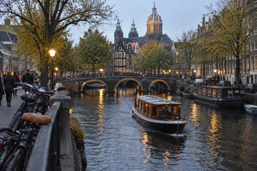 Amsterdam canal at evening with lit bridges and a moored saloon boat passing