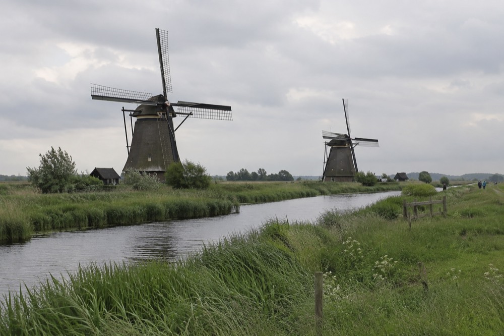 Two drainage windmills standing in a row across a flat green polder landscape with a waterway between them