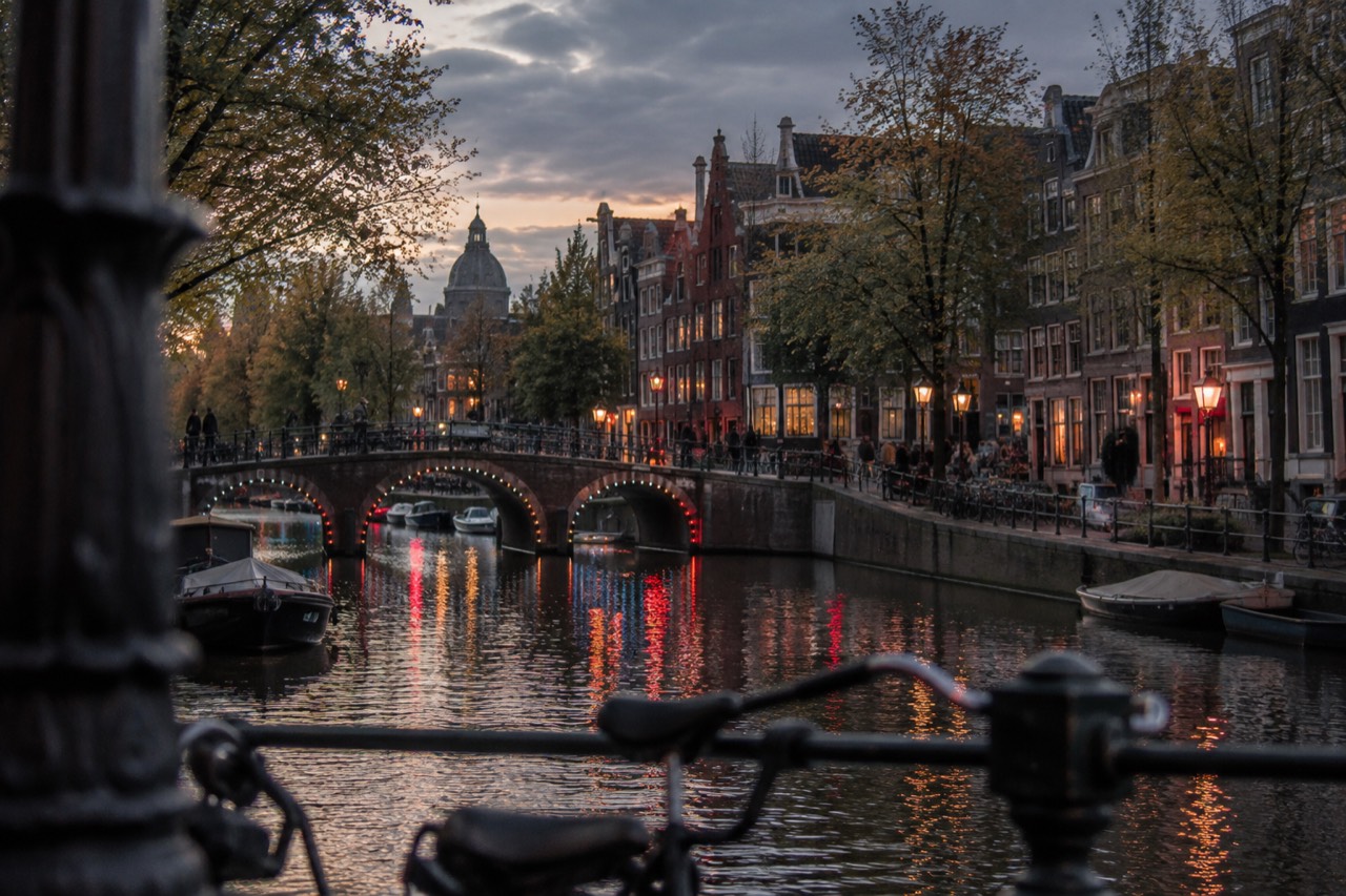 Canal houses and a bridge lit by red and white evening lights over an Amsterdam canal