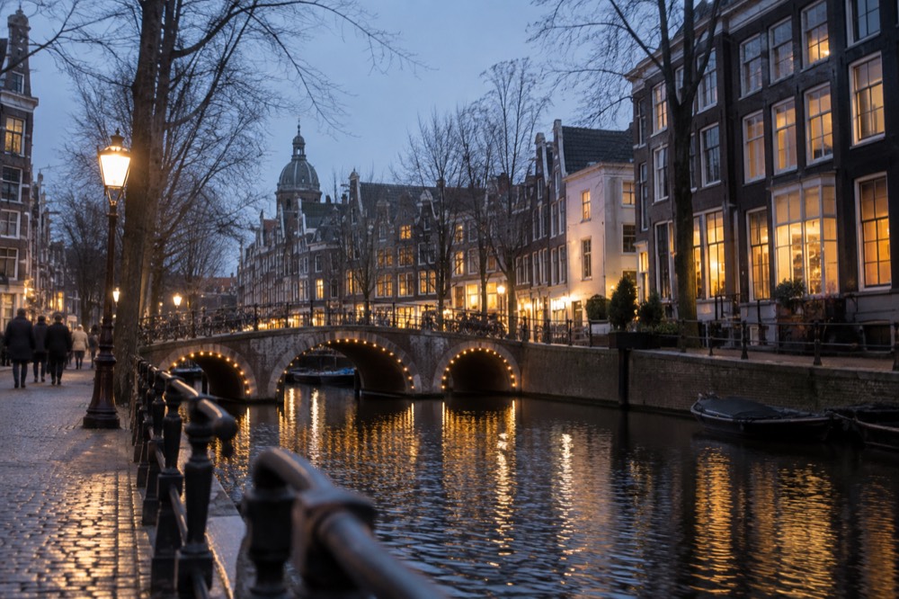 Canal-side shopfronts and a stone bridge along a quiet Amsterdam side street