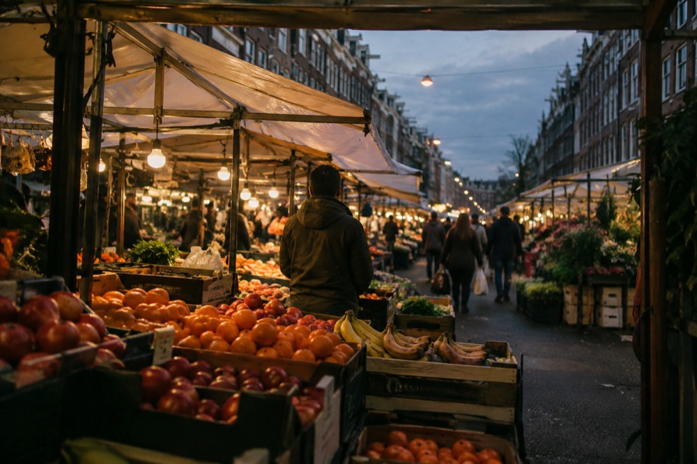 Rows of market stalls with fruit crates and canvas awnings on a busy Amsterdam street