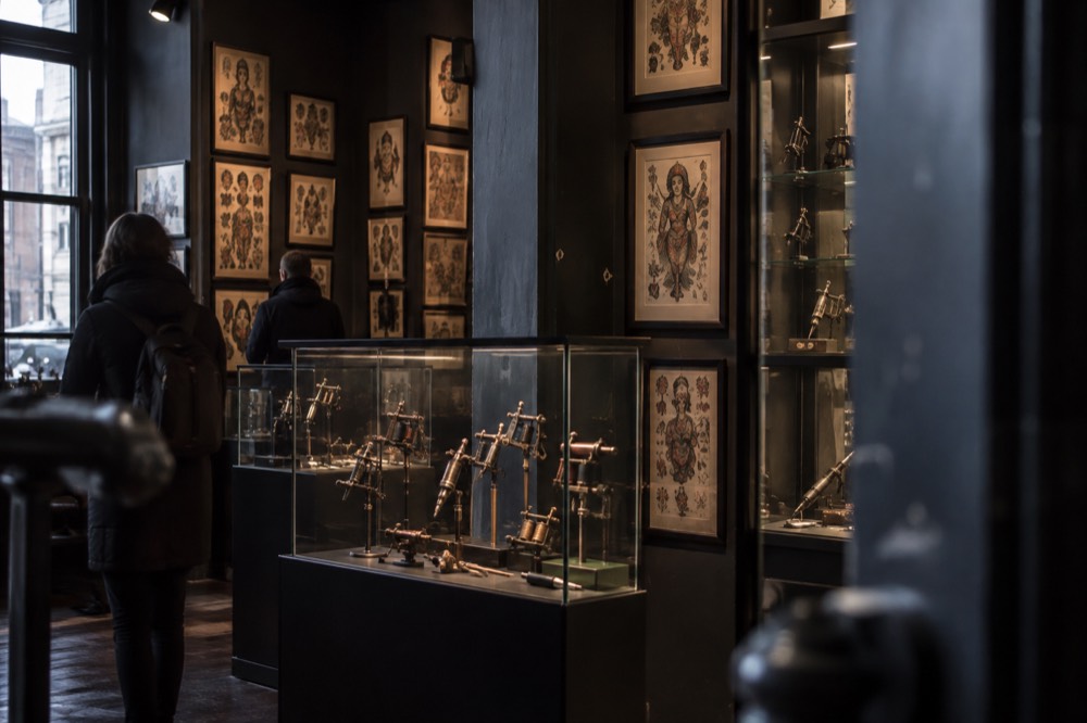 A display of vintage tattoo machines and framed flash art in a dim museum room