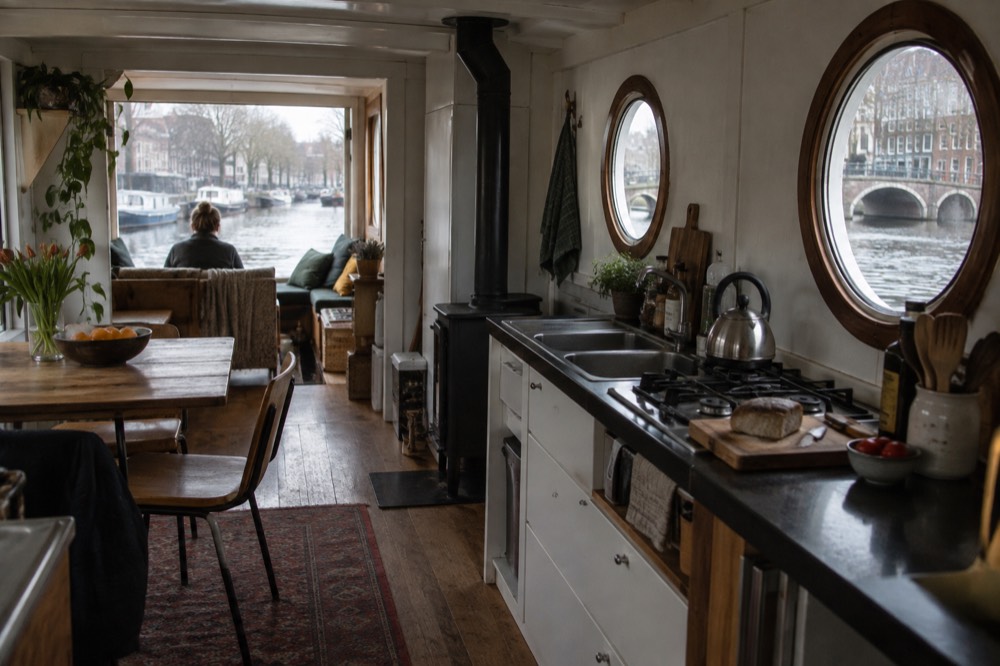 The interior of a canal houseboat with a small kitchen and porthole windows