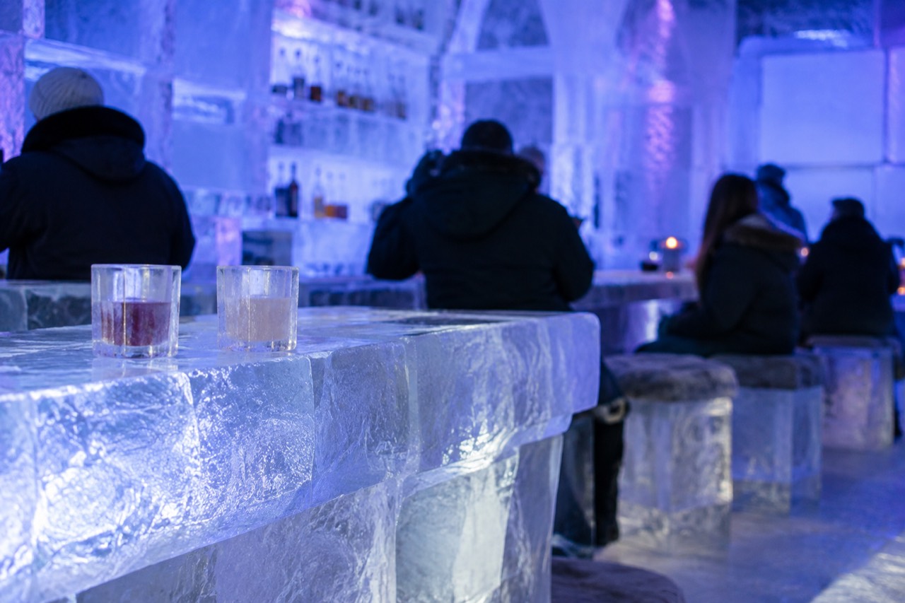 An ice bar interior with walls, benches and drinking glasses carved from ice, lit in blue and purple light