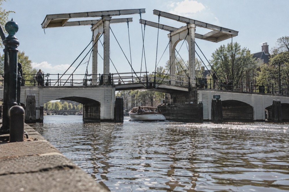 The white wooden Magere Brug seen from the Amstel quay with a small boat passing under it
