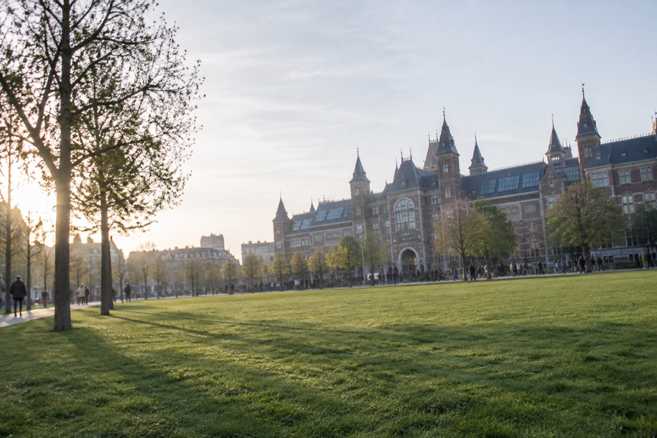 A wide green lawn in front of grand museum buildings under a bright sky