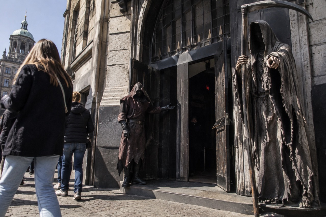 The entrance of The Amsterdam Dungeon on Rokin with a grim reaper statue and a costumed figure holding the door.