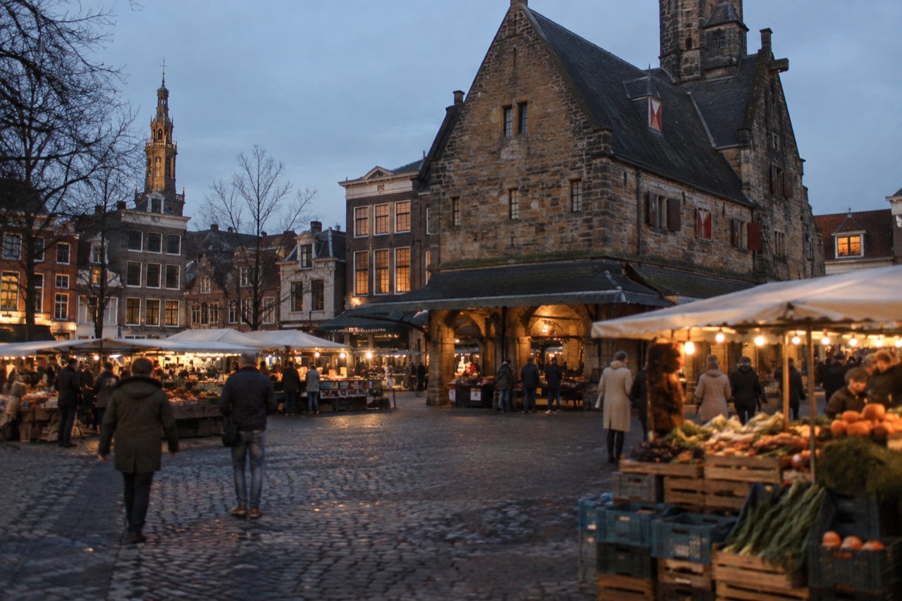 A historic Dutch square with a stone weighing house and market stalls under clear morning light