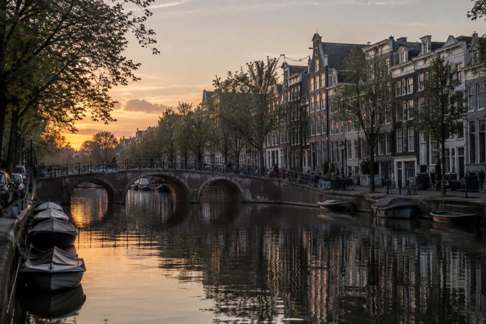 Canal in Amsterdam at dusk with a bridge and narrow gabled houses reflected in the water