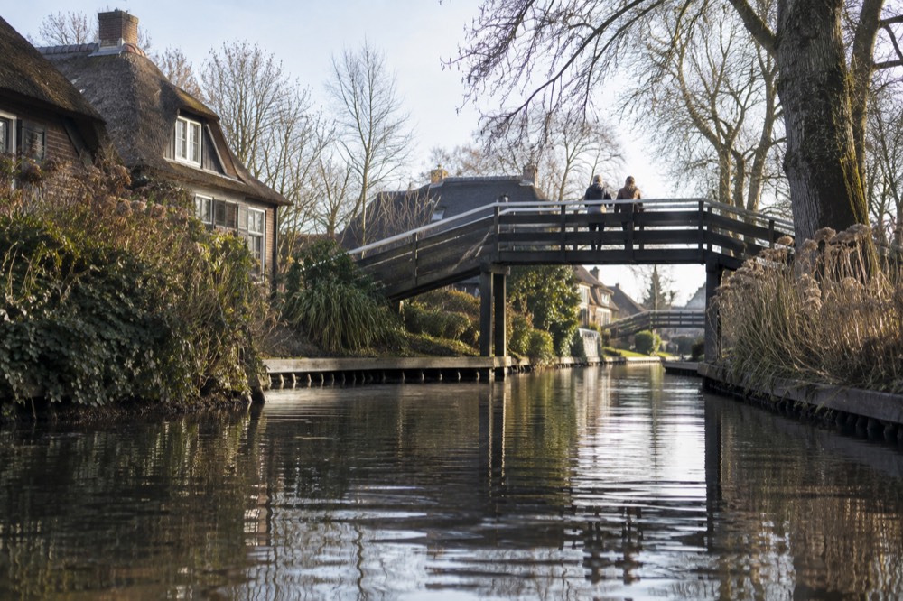 A wooden footbridge crossing a narrow Giethoorn canal between reed-covered banks