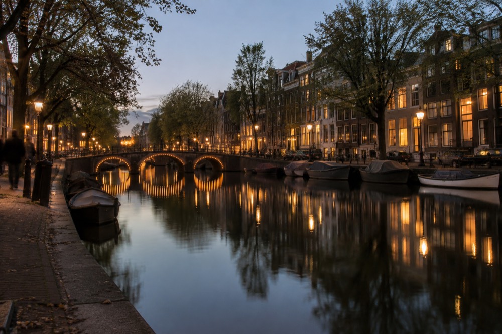 A canal in Amsterdam at dusk with bridges and lit facades reflected in still water