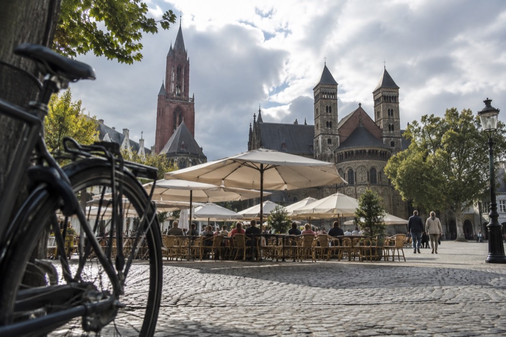 Wide stone square in Maastricht with two church towers rising above cafe terraces