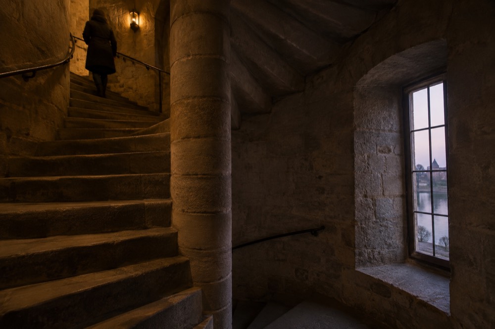 A spiral stone staircase inside a castle tower lit by a narrow window