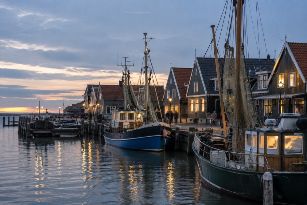 Fishing boats moored along a village quay with timber houses in soft evening light