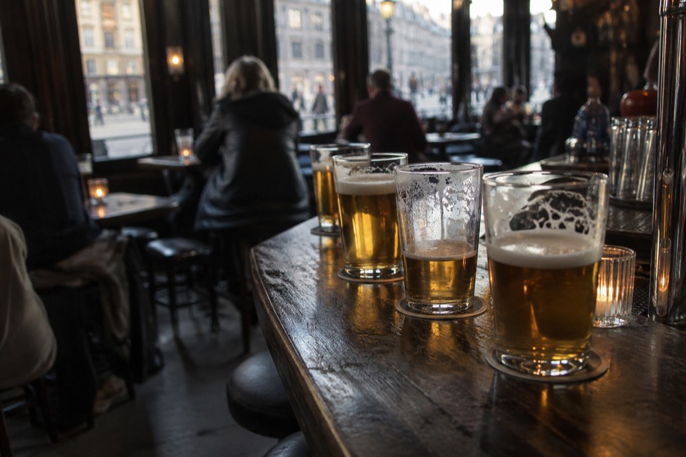 A row of beer glasses on a dark wooden bar in a low-lit Amsterdam pub