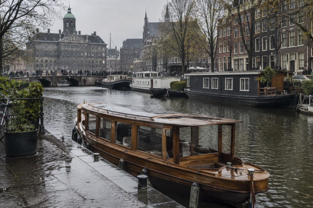 A wooden saloon boat moored beside a canal with houseboats in the background