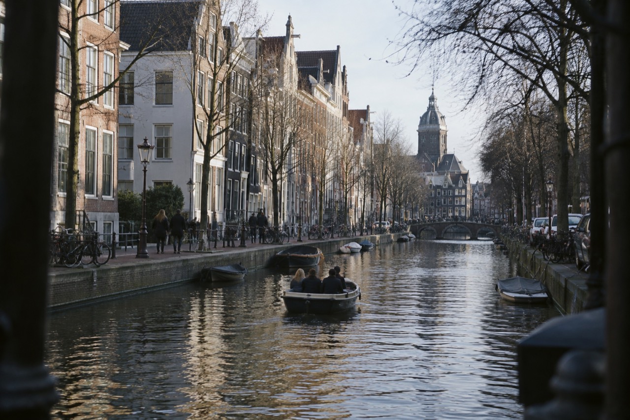 A small open boat cruising a tree-lined Amsterdam canal past gabled houses
