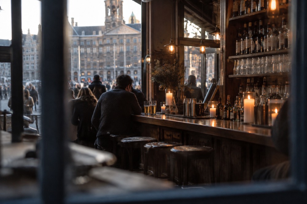 A candle-lit wooden bar counter with beer glasses and jenever bottles on shelves
